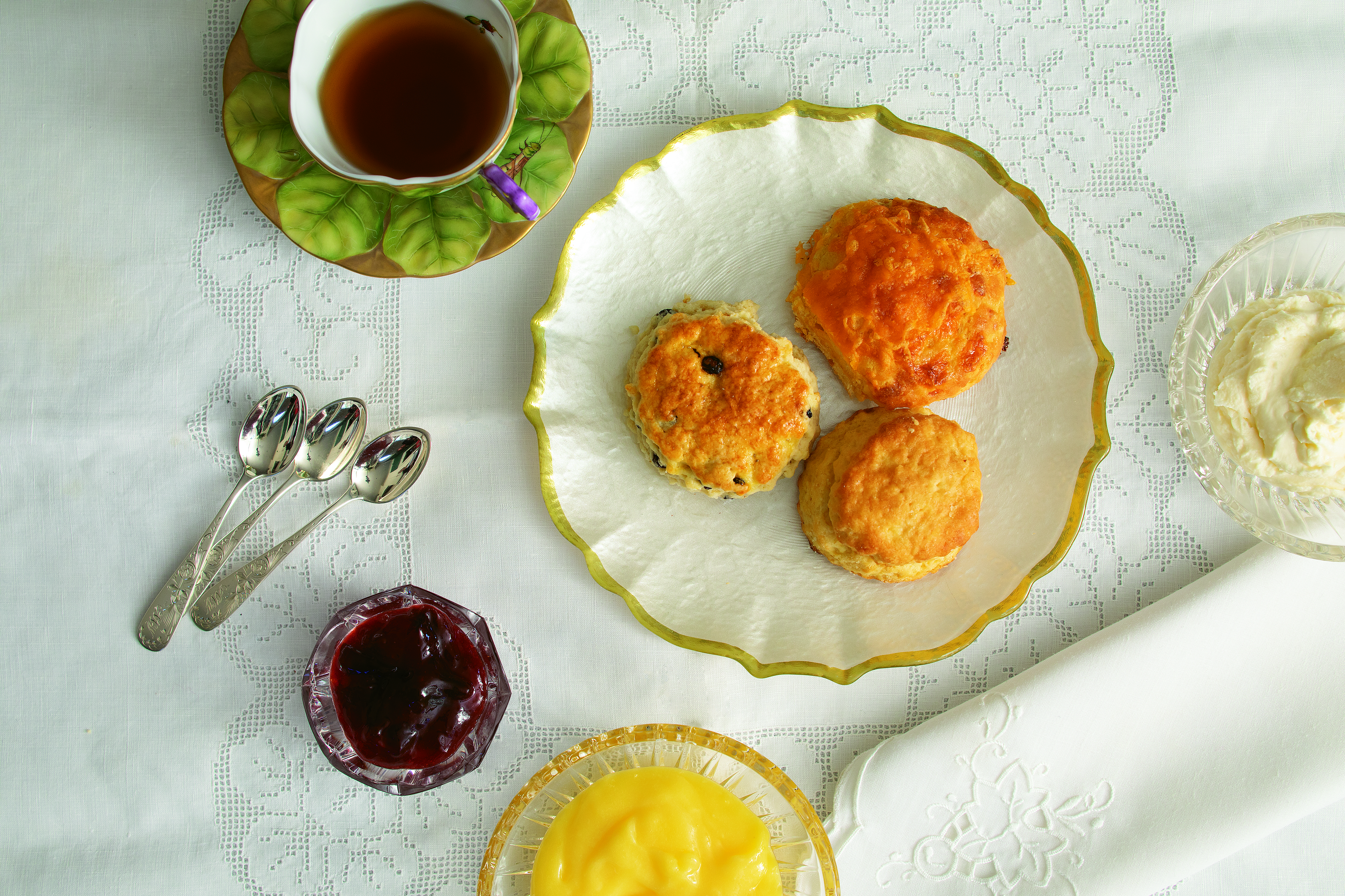 Sumptuous cheese, plain, and currant scones are served with clotted cream, luscious lemon curd, and strawberry plum jam. Hand-painted Anna Weatherly cup and saucer, plate and jam bowl from non(e)such.