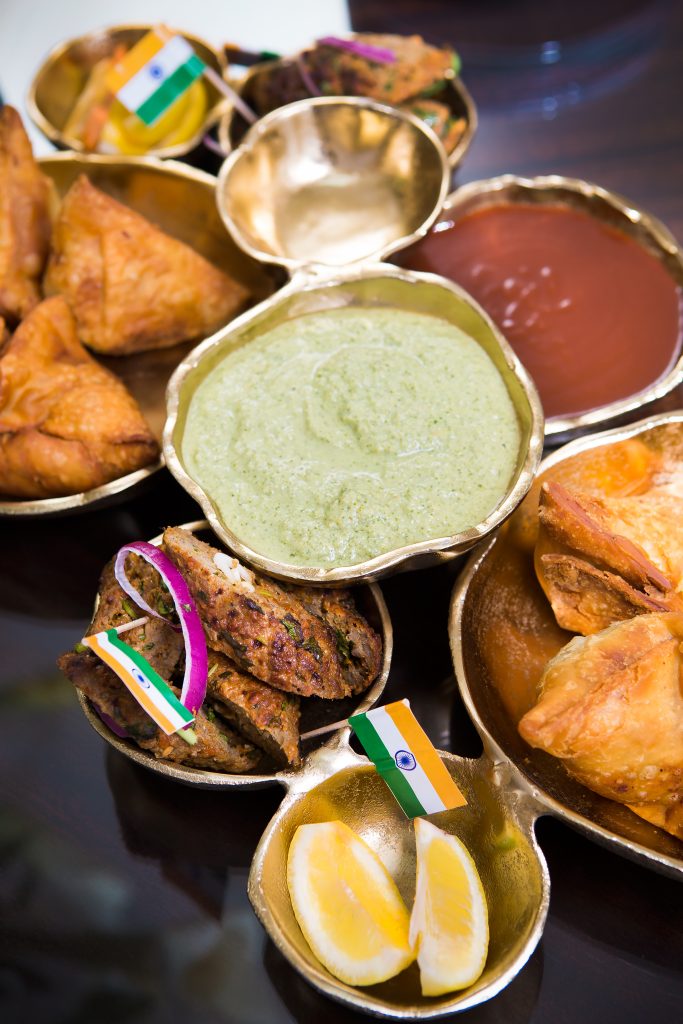 Samosa appetizers with lamb kebabs are artfully prepared by Bhavna and served with decorative waves of the national flag of India, a rectangular tricolor of India saffron, white, and India green with the Ashoka Chakra, a 24-spoke wheel at its center. 

