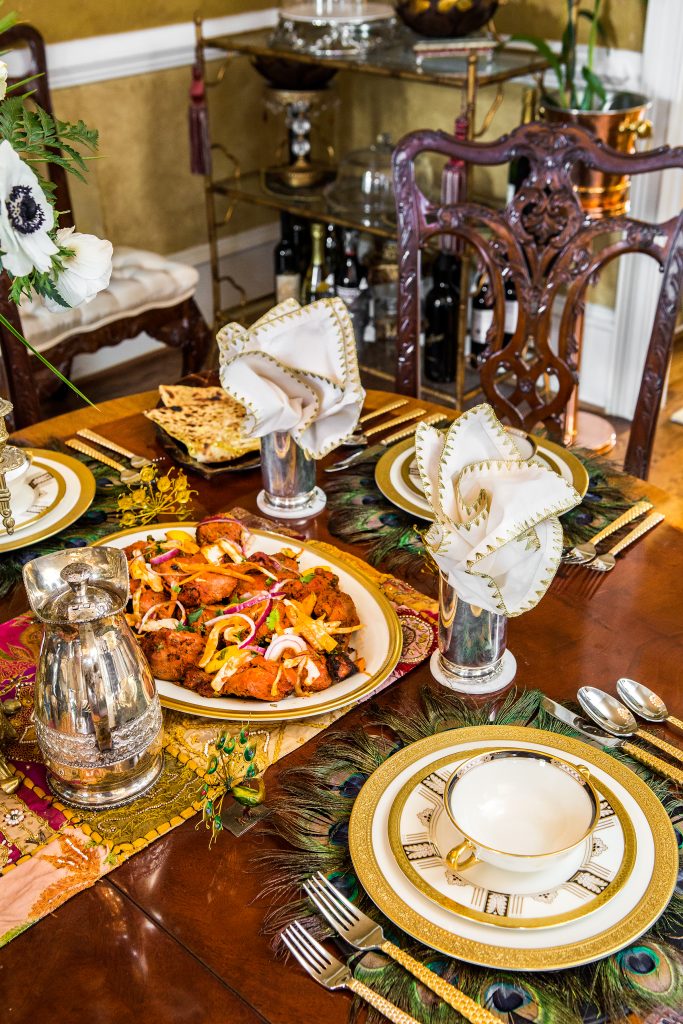This elegant luncheon that Bhavna prepared includes Tandoori chicken and naan bread. Lenox gold and white china rests on placemats accented with peacock feathers. Sterling silver pitcher and water glasses with Michael Aram flatware reflect a sophisticated table. 