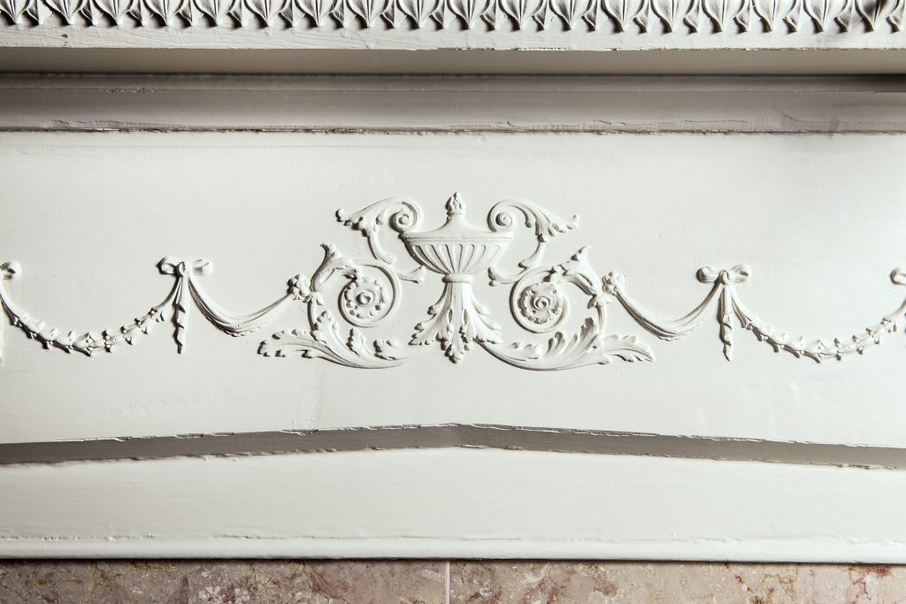 The fireplace has a beautiful decorative neo-classical urn with scrolls and flowers. 