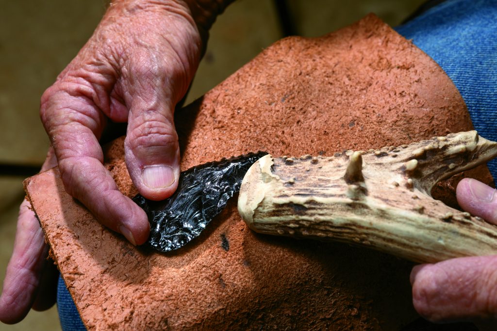 Marty uses the base of a white-tailed deer antler to break off a piece of obsidian, a naturally occurring volcanic glass. He then begins to knap it into an arrowhead, using the antler tip for the final stages.