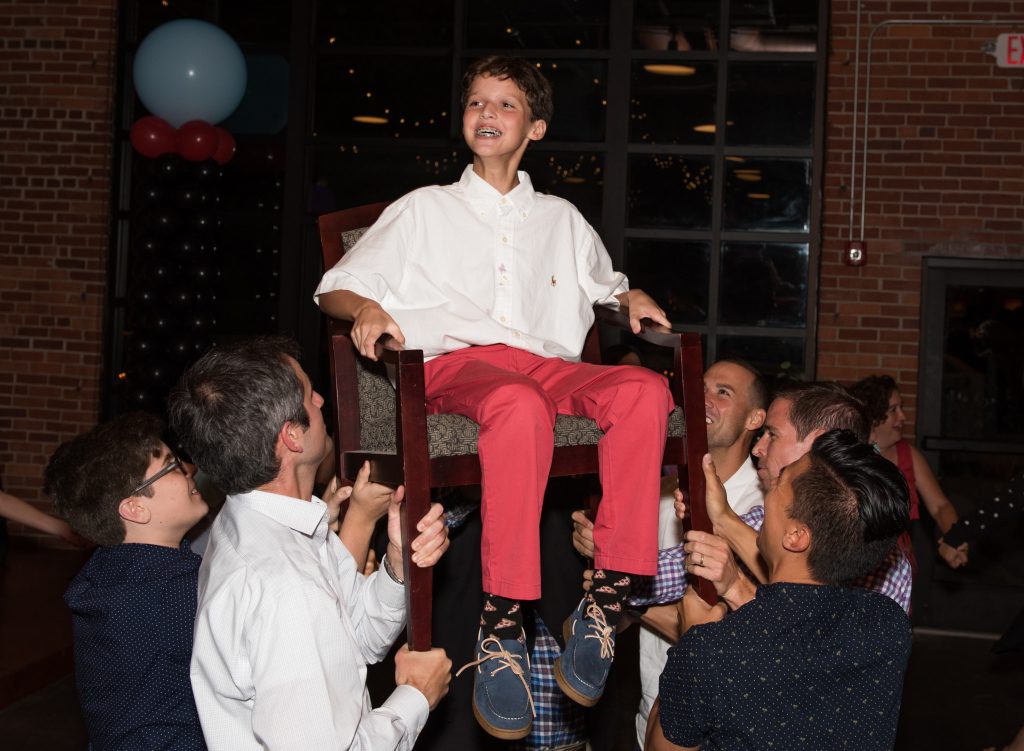 At his celebration on Saturday night, Sam is raised in the air by his family and friends in the middle of the traditional dance called the hora. The group dances in a circle to celebrate his achievement of becoming a bar mitzvah. 
