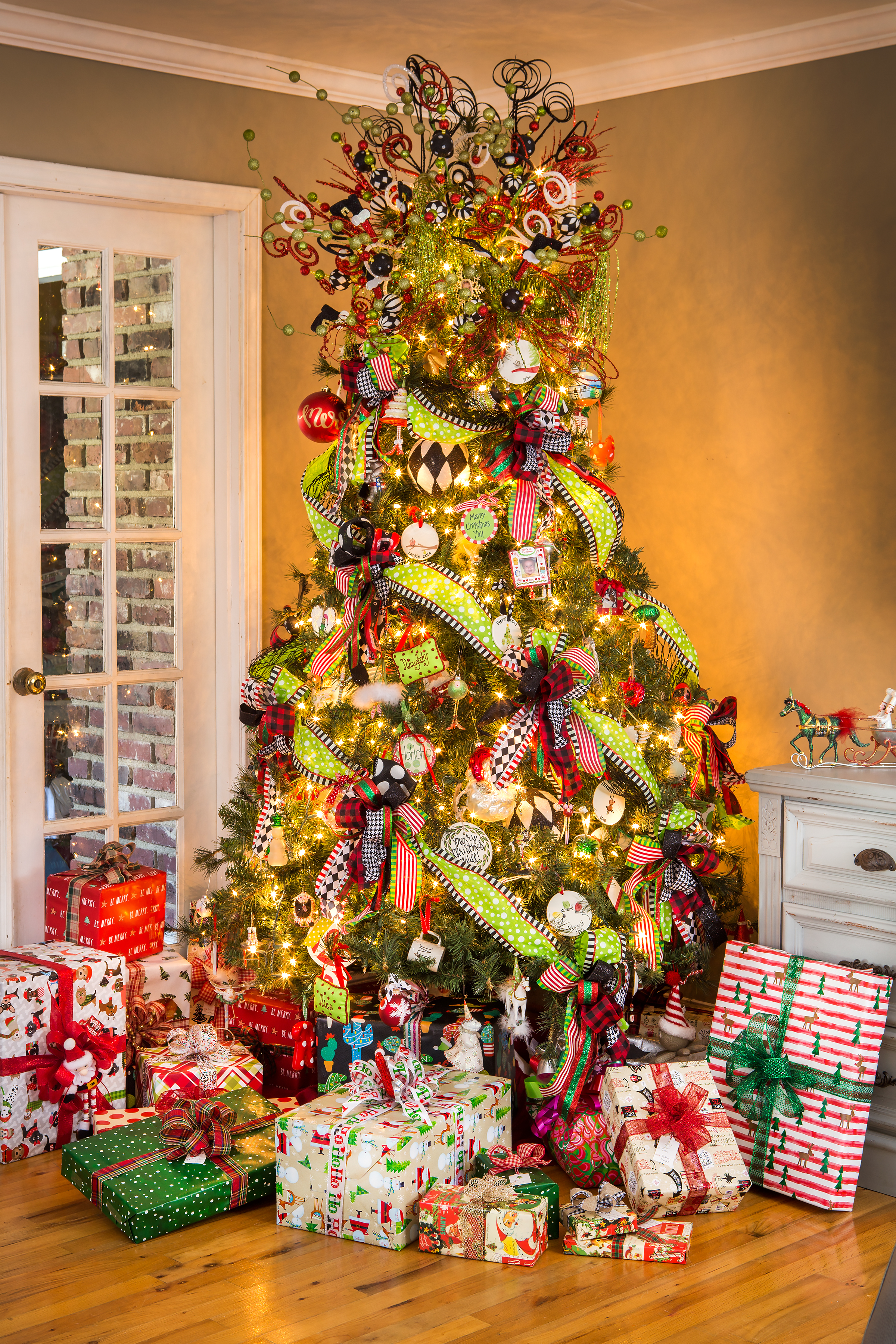 Karli and Gabriel Reynolds’ Christmas tree is inspired by Dr. Seuss’ whimsical, crazy, colorful children’s books. For the past five years, Karli has used a theme of lime green, black, and red with her artificial tree, but she says it is always evolving. Karli does all the decorating herself, often traveling to stores like Carolina Pottery to create the explosion of color with bows and ribbons that sprays across the tree from top to bottom. Perfectly wrapped gifts are placed for color and balance. Handmade ornaments by her two children, Pressli, 9, and Larkin, 6, give the tree a personal touch.  