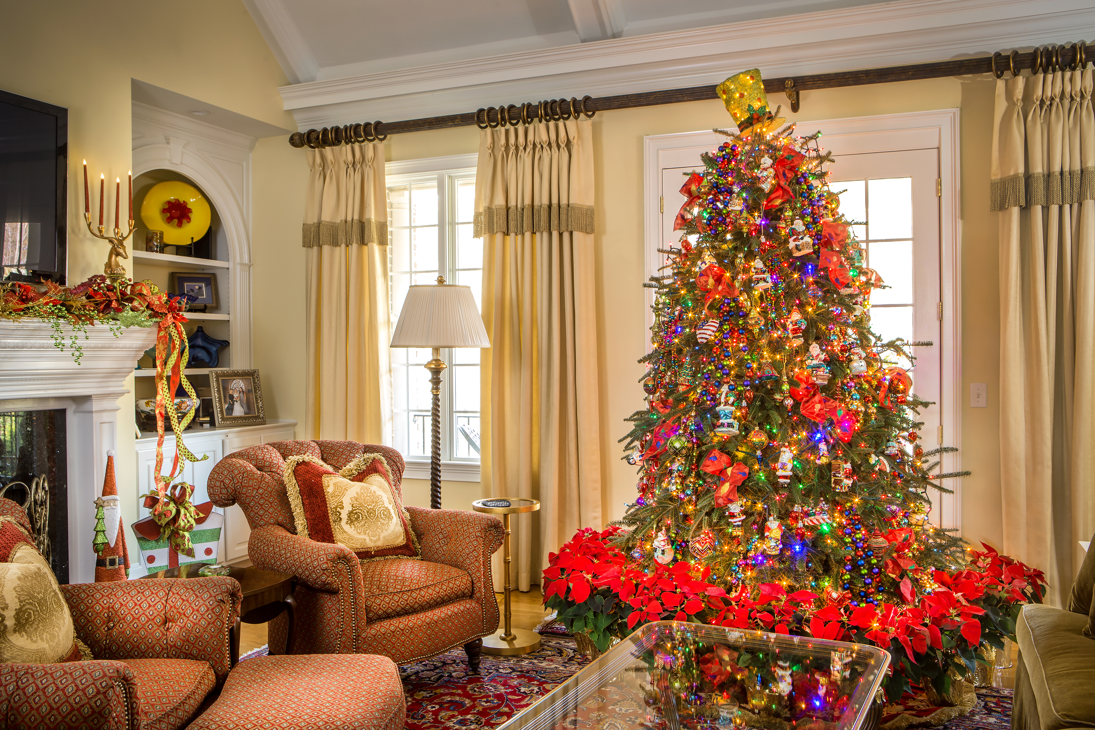 Donna Strom’s home is blessed to have floral artistChad Ridenour decorate for the Christmas season. Her glorious tree is centered in her living room by the fireplace with all new glass ornaments, acquired since the 2015 flood, mostly made by Mark Roberts and Christopher Radko. The skillfully handcrafted, collectable Radkos are Polish-made, featuring favorite Christmas symbols and exclusive Radko themes. Mark Roberts’ ornaments are complementary collectible jewels that sparkle and shine. This year the tree features blinking lights for the first time and a ring of red poinsettias around the base of the tree, both added by Chad. 