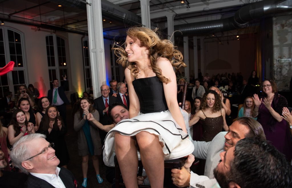 Kacy being lifted in a chair during the hora dance. The hora is a Jewish traditional celebratory dance performed at weddings and bar/ bat mitzvahs, typically danced to the music “Hava Naglia.”
