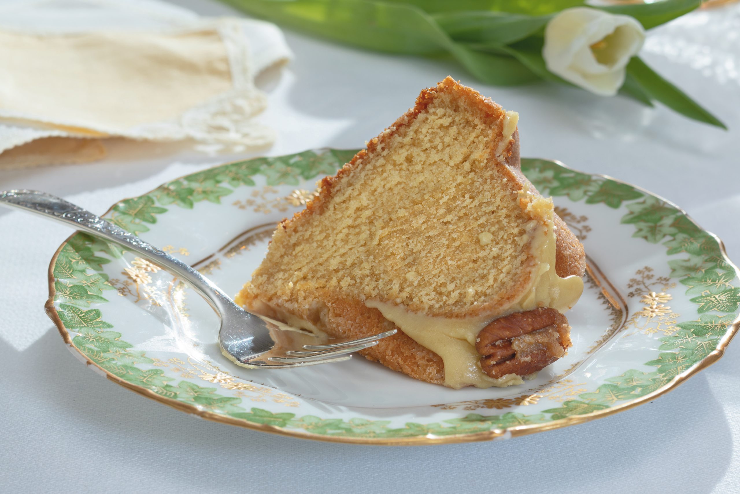 A slice of Ed’s Favorite Pound Cake, served on an antique Limoges plate, is coated with a rich molasses glaze and decorated with glazed pecans. 