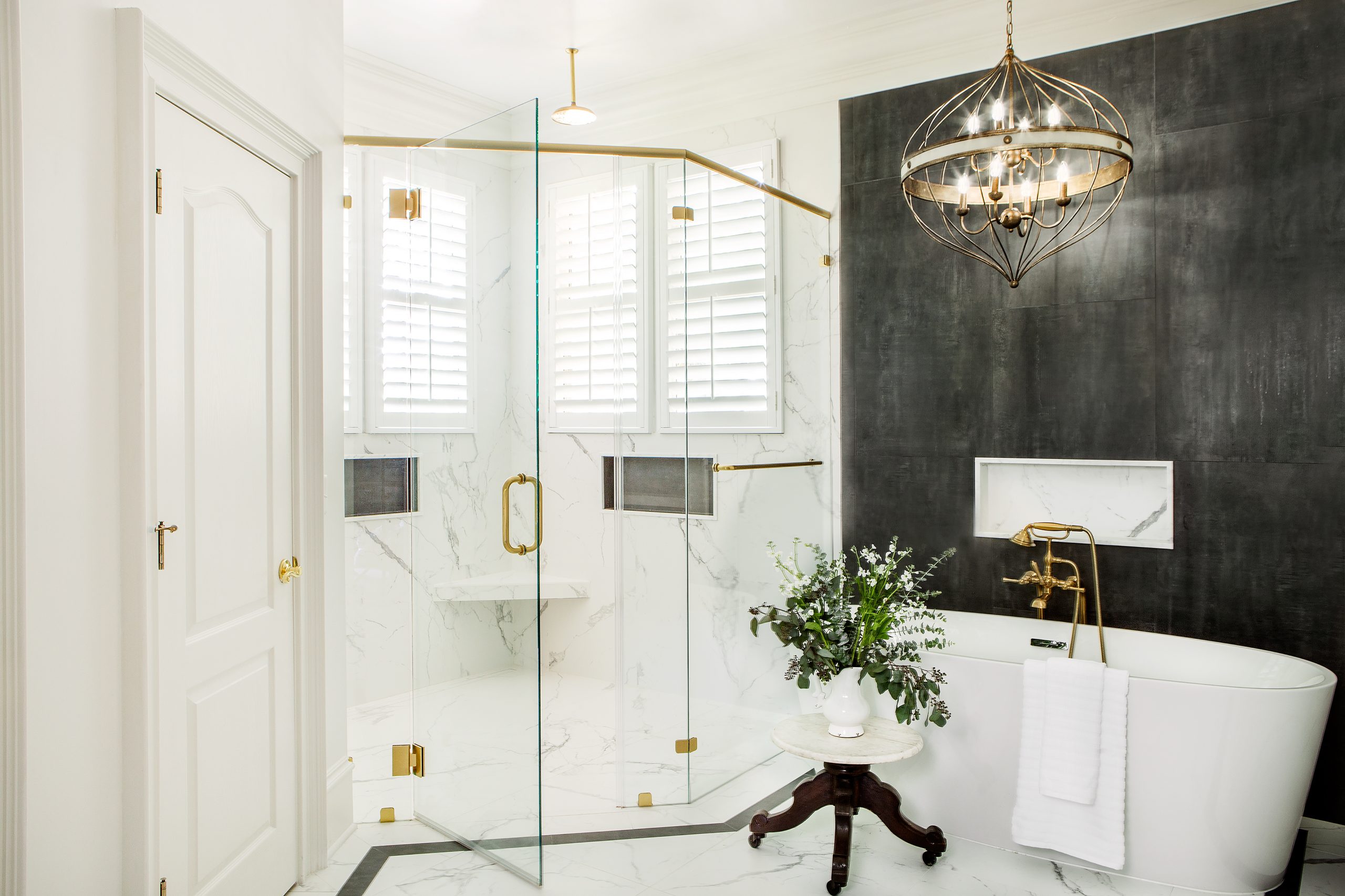 A deep soaking tub next to a wall of dark tile selected by Veronica from Palmetto Tile, accented by a modern chandelier, is the focal point of the gracious master en suite bath.