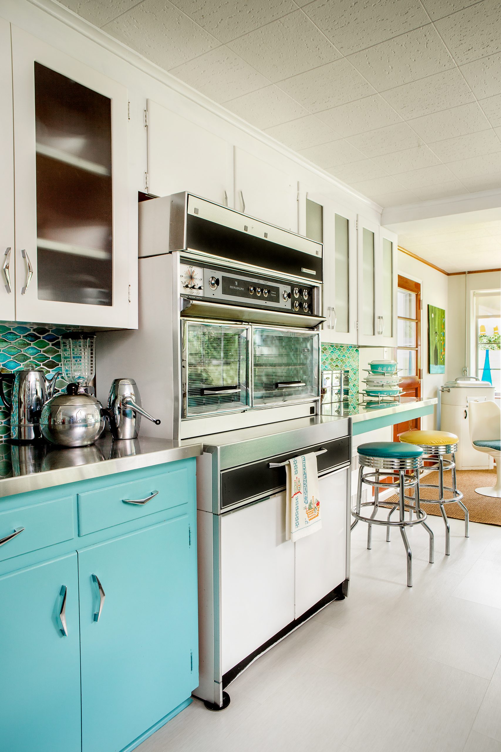 The kitchen is lined with cabinets original to the home, accented by colorful turquoise glass tiles in a geometric pattern by Hirsch. The oven range, found on eBay, is interestingly the original Frigidaire version as seen on the sitcom Bewitched!