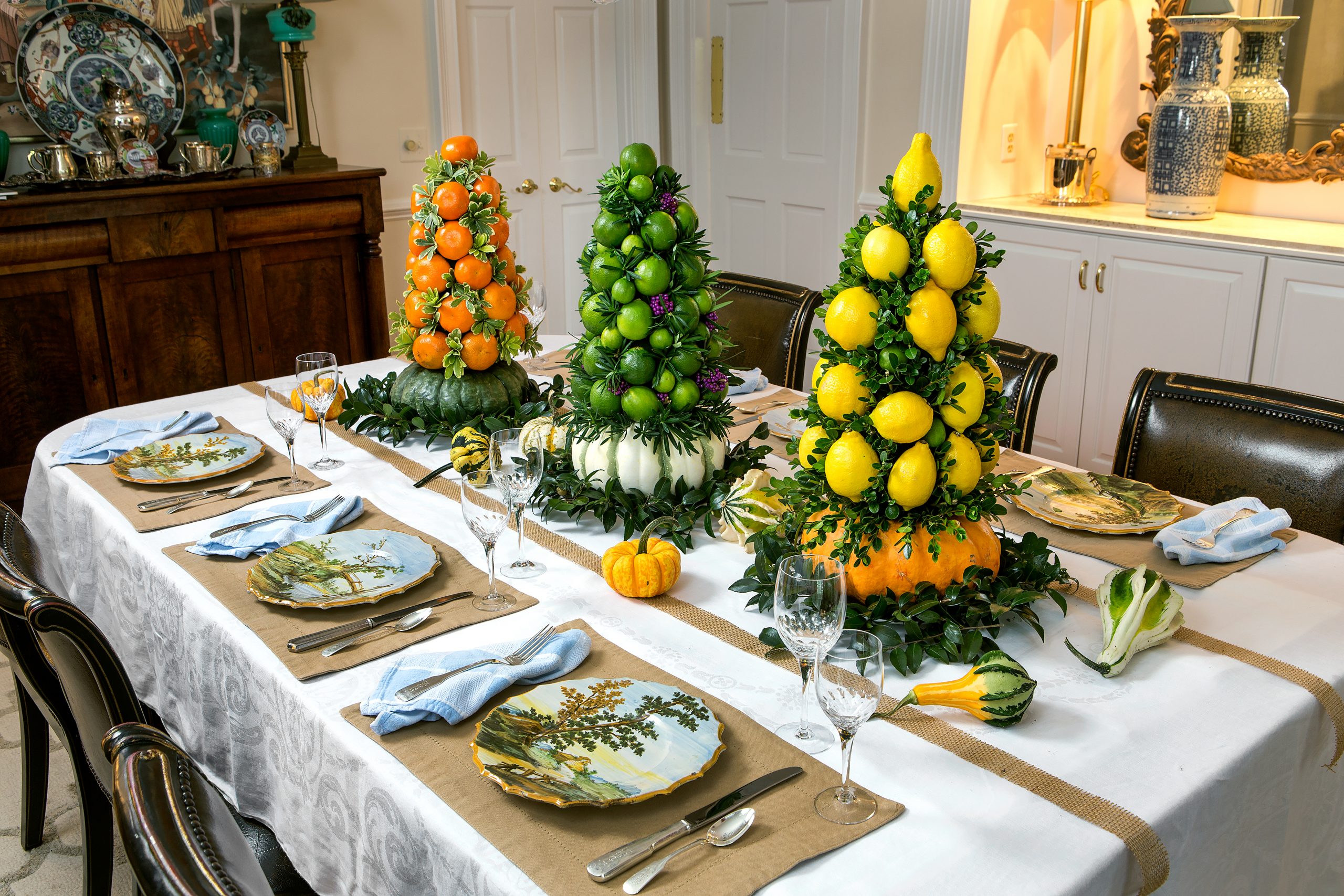 The addition of pumpkins to the base of the fruit topiaries, small gourds and burlap runners across the table, and a more casual set of placemats and napkins transform the formal table to a more rustic holiday setting. 
