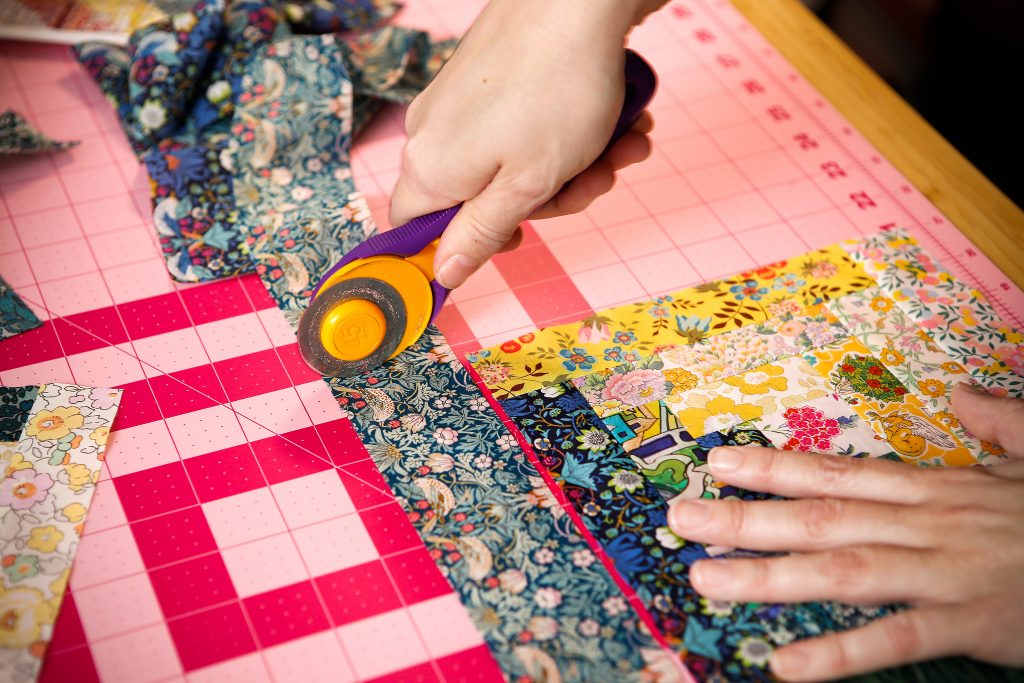Kristy uses rotary cutting, which does not involve scissors, to cut fabric on a mat.