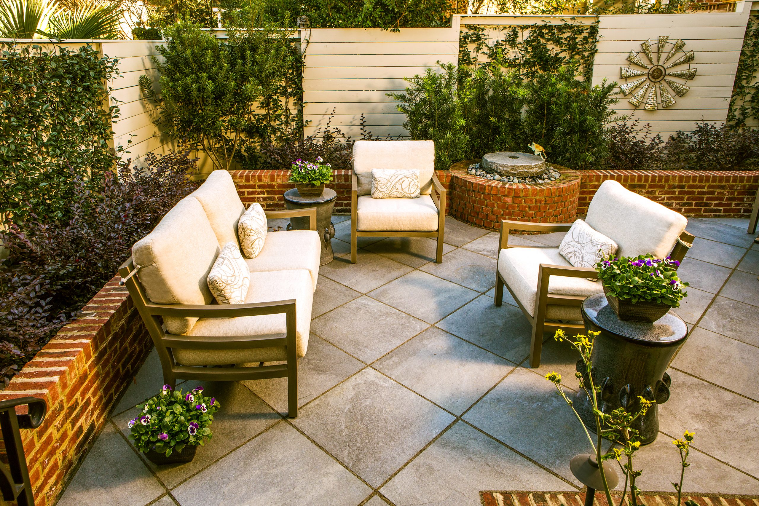 With the design help of Mark Cotterill of Grimball Cotterill Landscape Architects and Steven Ford, Della designed her back courtyard to create solitude and privacy. At the bottom of the steps, a comfortable seating area awaits by the lime tree her children — Alan, Kallie, and Zachary Eisenman — gave her for Mother’s Day. A low red brick wall defines planting beds backed by a shiplap fence, softened by a round metal sculpture. While the garden has many beautiful features, the fountain made of thick granite millstone is one of her favorites. 
