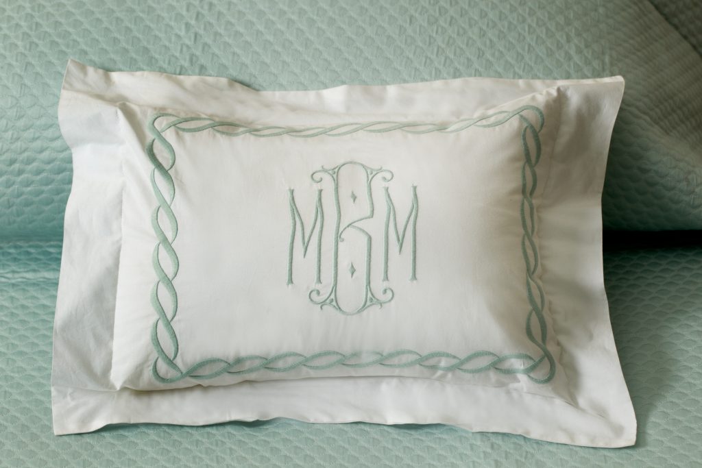 Make a luxurious Matouk bed with a light blue coverlet accented with an elegant pillow trimmed in a chain stitched border, traditional style monogram. 