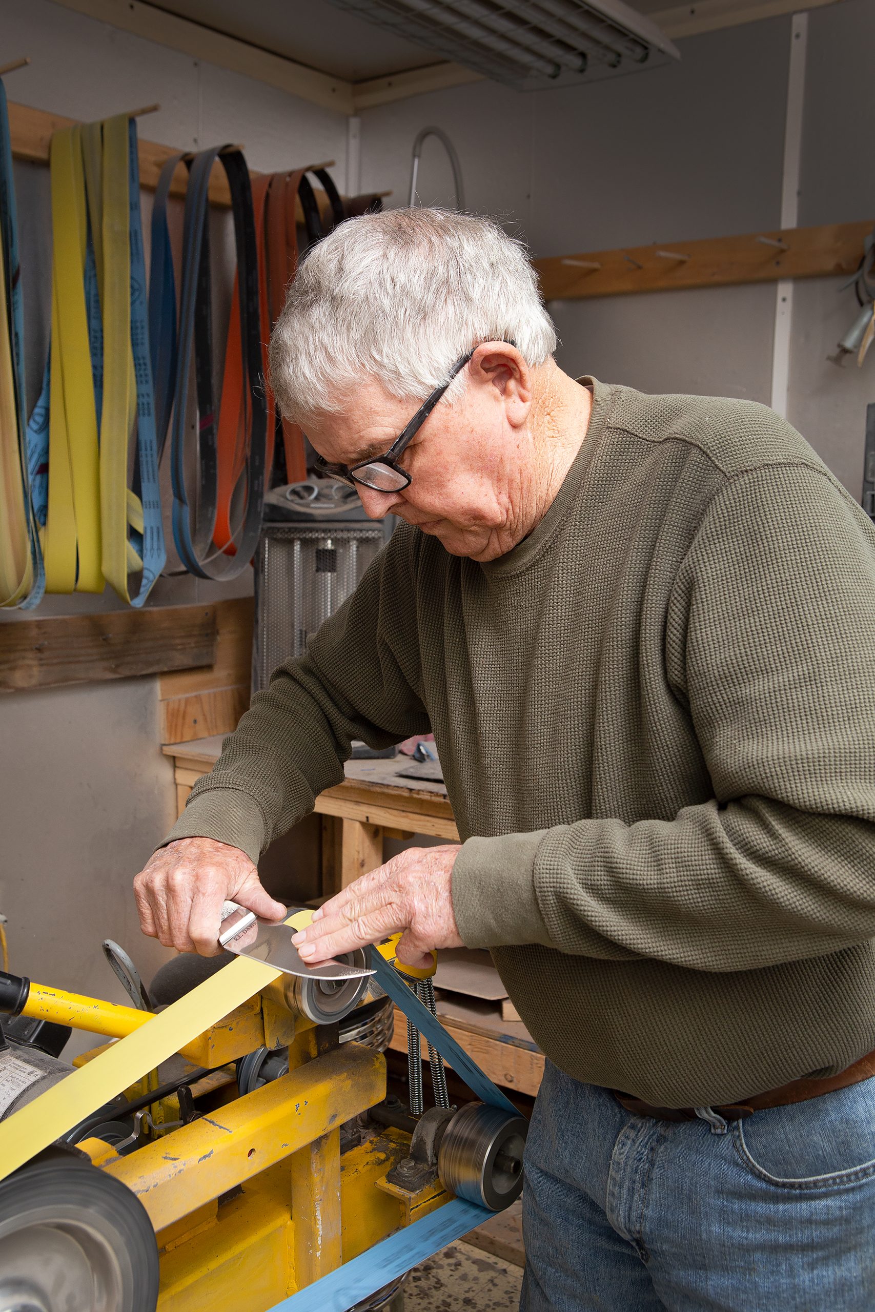 Working at the sander, Robert cuts down, shapes, and polishes the blades and handles of his knives. 
