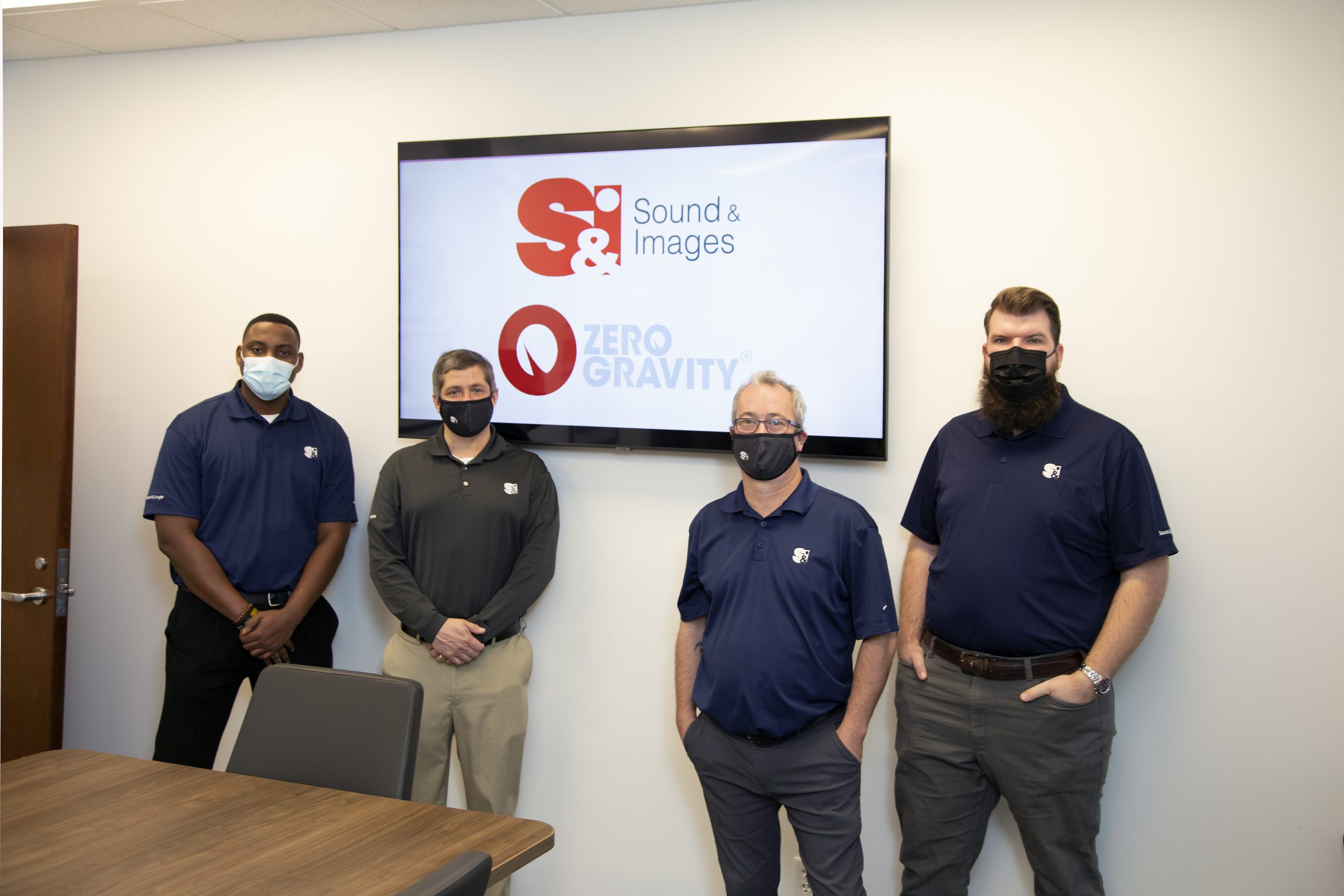 Ismail Lee, Adam Vance, Rodney Wallace, and Logan Hacker in front of an S&I conference room monitor installation.