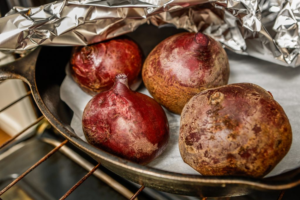 One way to prepare roasted beets is to cut off the leafy tops, scrub the skin with a brush, place them in a cast-iron skillet on parchment paper, cover tightly with foil, and bake in a 400 F oven for approximately one hour. 