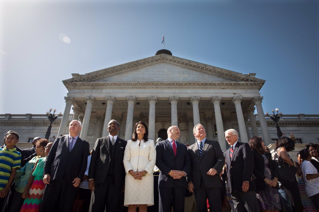 Gov. Jim Hodges; the Rev. Norvel Goff, interim pastor of Mother Emanuel AME Church; Gov. Nikki Haley; First Gentleman Michael Haley; Gov. David Beasley; and Charleston Mayor Joseph Riley watch as the Confederate battle flag is removed from the South Carolina State House grounds in July 2015. Photography by Zach Pippin