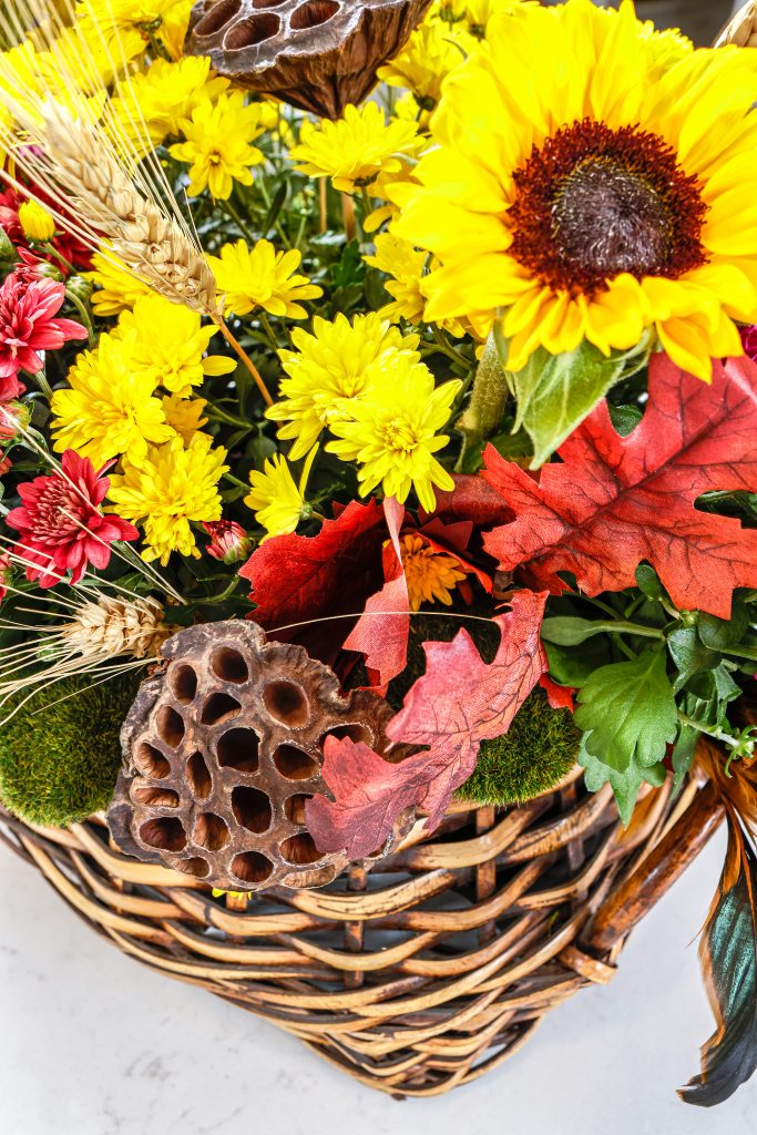 Creating a centerpiece in a basket is easier than you think. Gather seasonal flowers, like mums, in small containers and artfully combine them in a suitable basket with a wide opening. Having the flowers in their containers will make them easier to water. To add more interest, collect and cut extra stems like sunflowers, fit them with water as needed, and slide them into the arrangement. For diversity, add gourds, feathers, or greenery. Voila!