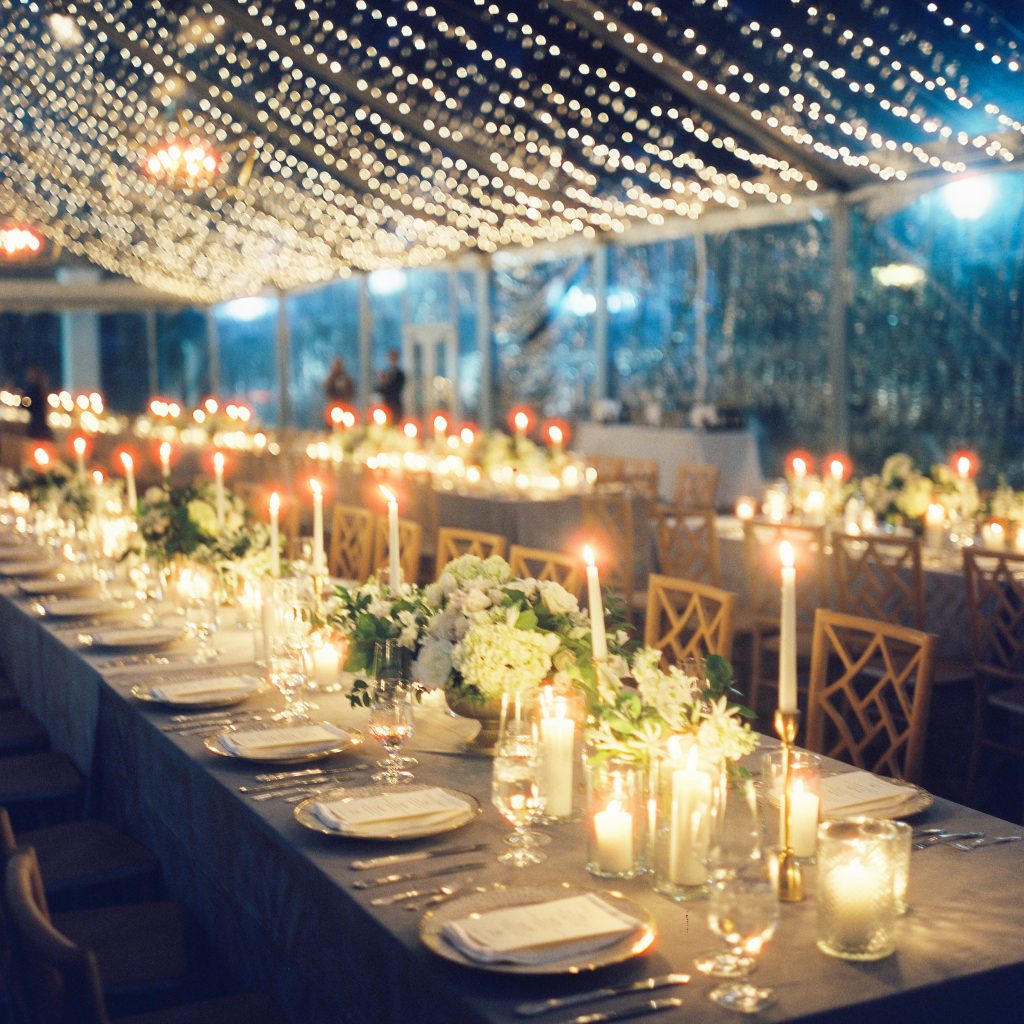 Blue velvet tablecloths with monogrammed napkins complement the timeless table setting of white lights, candles, and lush greenery. 