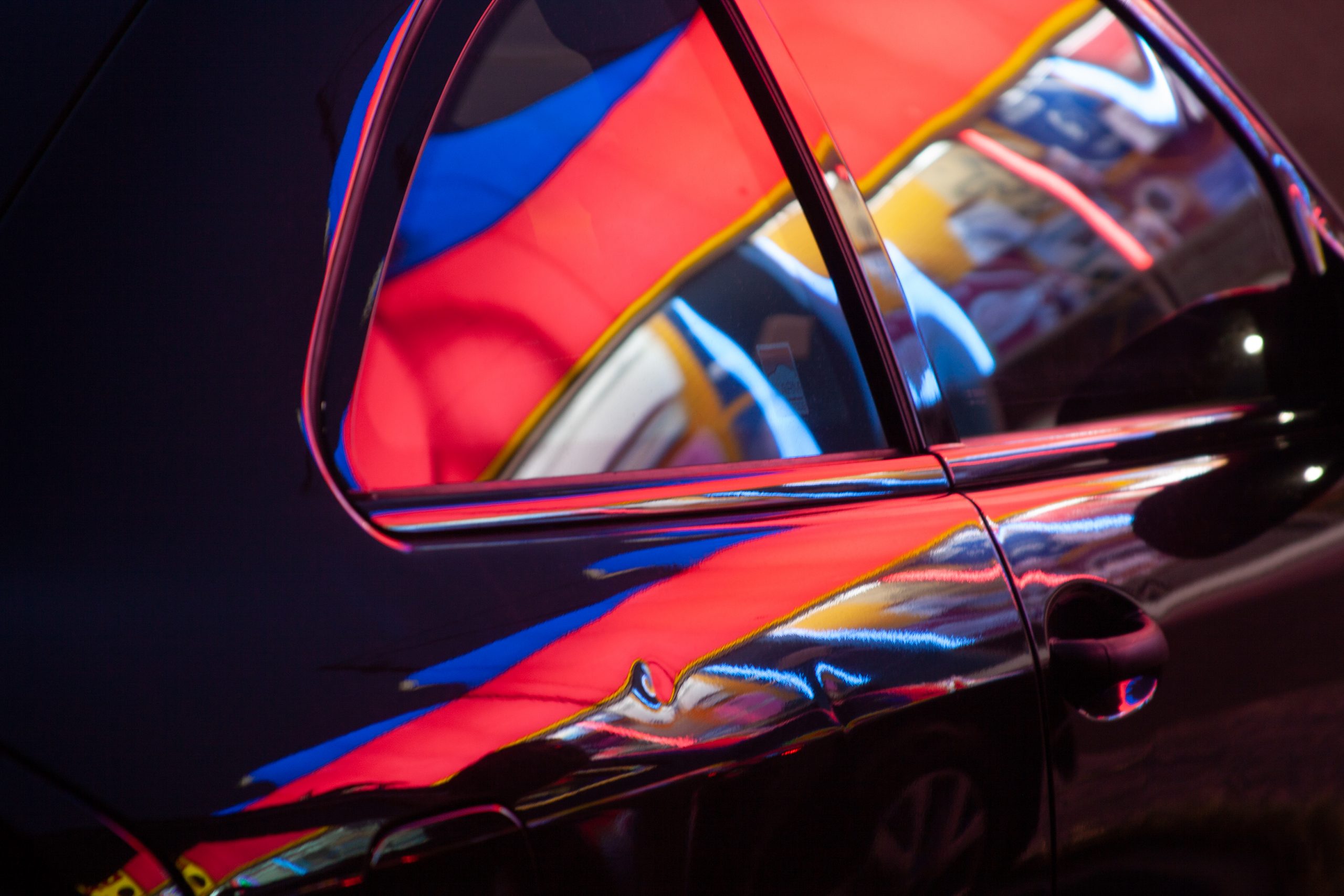 Neon color reflections create a vibrant abstract pattern on a patron’s car. 
