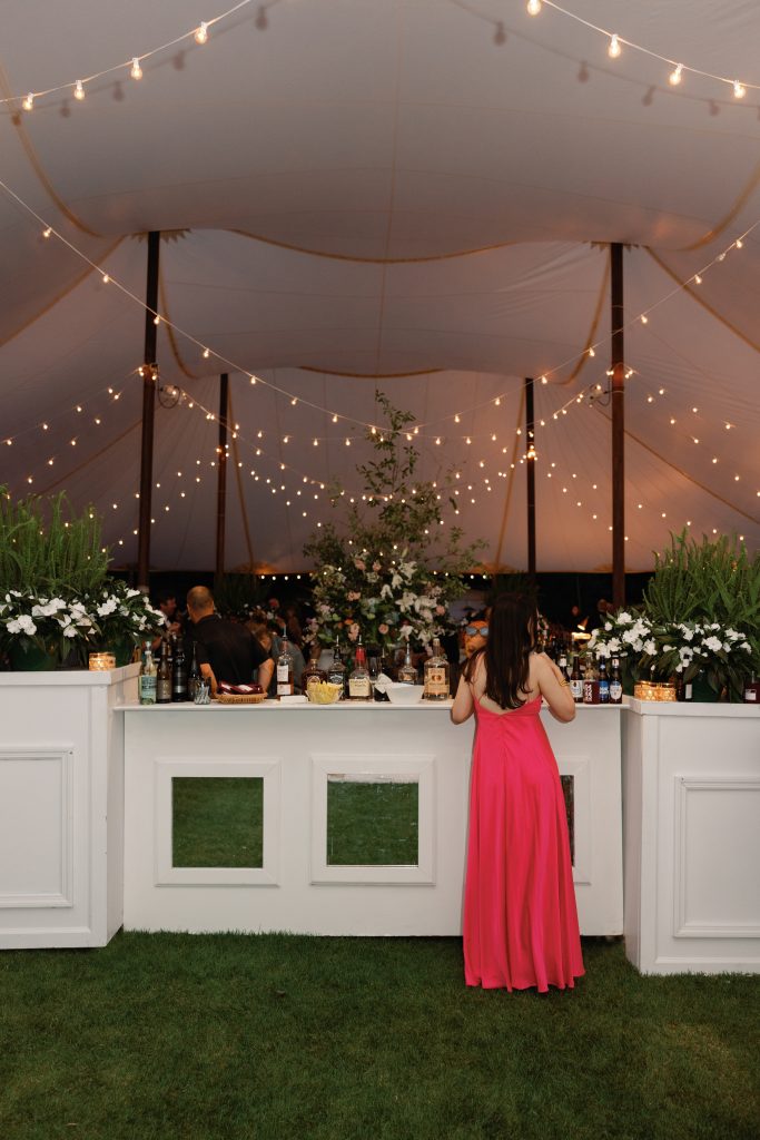 A grand square bar in the center of the tent accommodated eight bartenders. Julianne Sojourner counted on the fact that Fred and Lee Gantt own a landscaping company to bring in lots of ferns and blooming plants as part of her vision for the reception. Ambient Media Event Lighting provided market lights that glistened between tents to guide guests around the reception. 