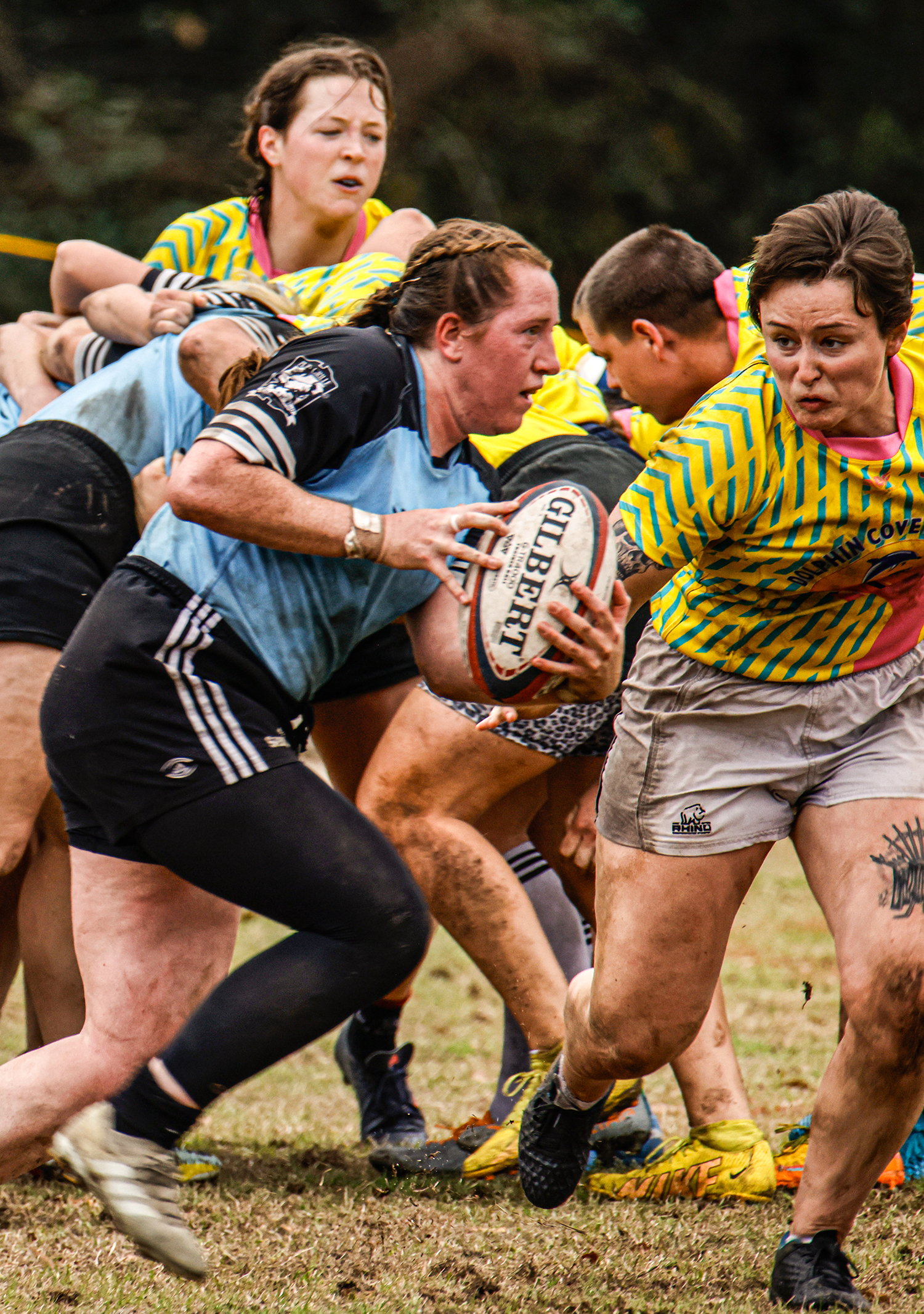 The back person in the scrum advances the ball as a scrum breaks up in the background.