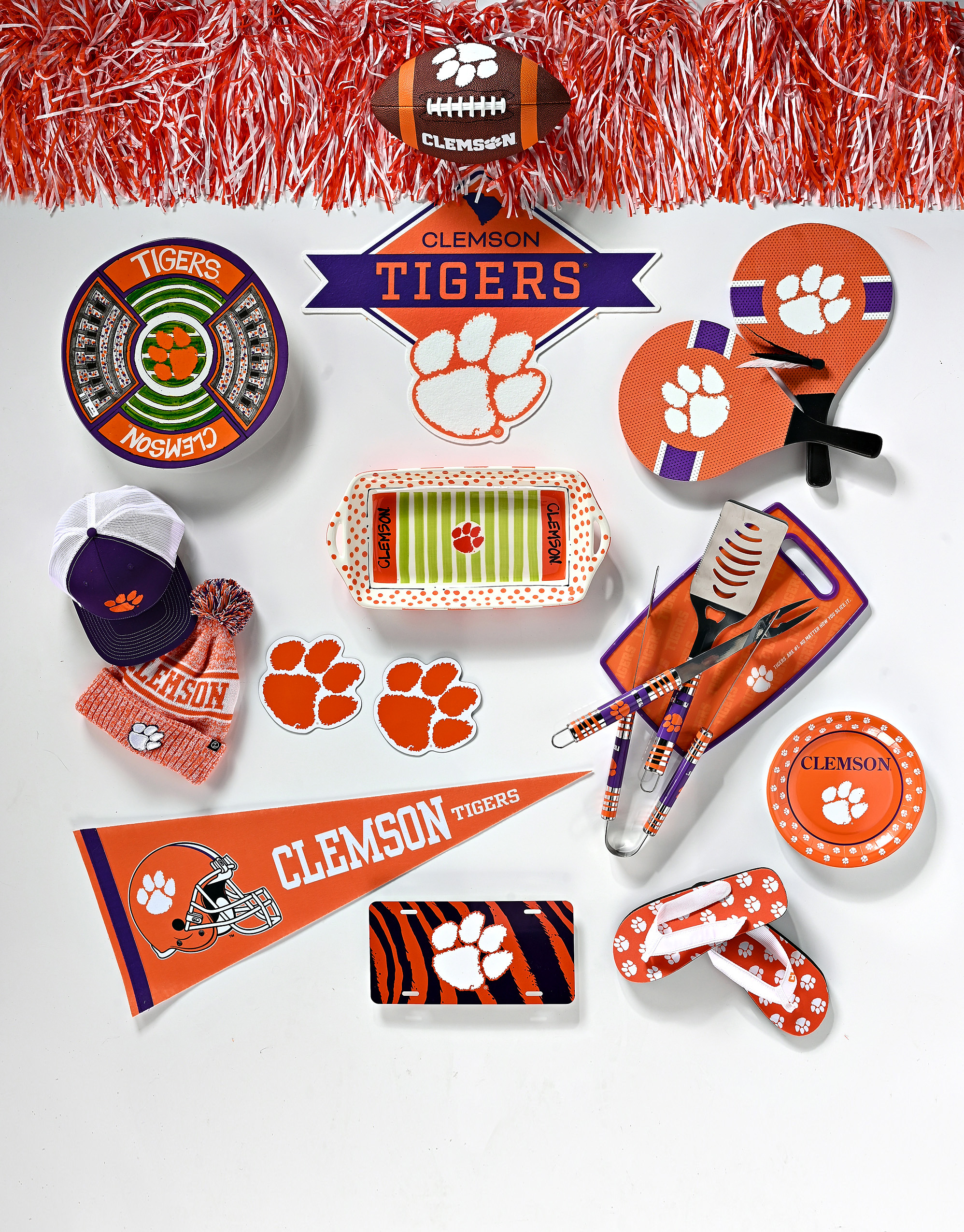 Clemson pompoms and air tech football, diamond-shaped Clemson logo, round and stadium platters, paddle birdie, magnetic orange paws, tiger tailgater 3-piece barbecue set, cutting board, and Clemson flip-flops courtesy of Clemson Traditions; Clemson pompoms, Richardson Clemson hat and beanie with puff, wall flag, 9-inch paper plates, and Clemson paw license plate courtesy of Todd & Moore.