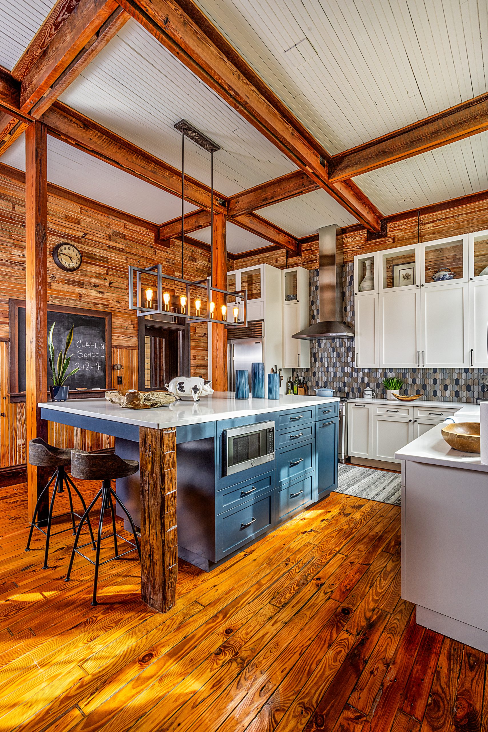  The kitchen is a chef’s dream with high-end appliances, a muted blue slate color scheme, a farm sink, and a massive island with quartz countertops. In honor of the building’s roots as an old schoolhouse, Ben installed a blackboard with chalk and an old-timey pencil sharpener.