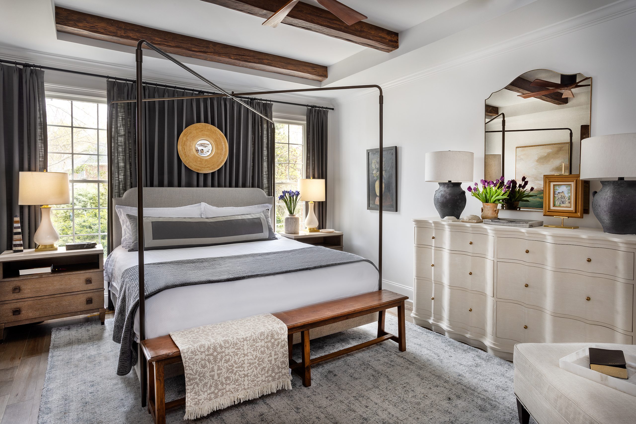 Dark gray drapes extend across the entire headboard wall behind the Palmers’ iron canopy bed, and dark wooden beams extend above the bed, recessed in the tray ceiling. The space is warm and inviting.